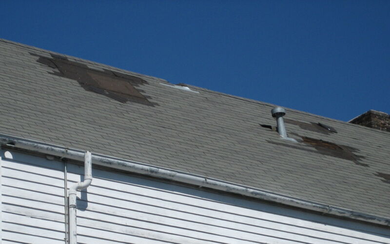 Aging residential asphalt shingle roof with missing and patched shingle sections, a sign it may need replacement