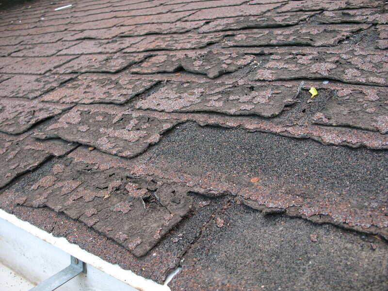 Close-up of worn, curling asphalt shingles that have failed and let water through