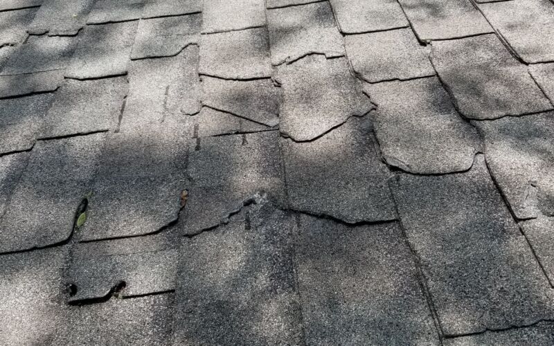 Storm-damaged asphalt shingle roof with lifted and missing shingles after high winds